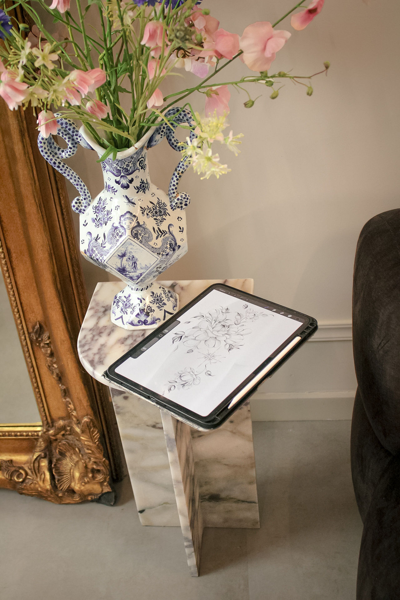 Een bloemenontwerp op een tablet op een marmeren standaard, naast een vaas met bloemen en een gouden spiegel